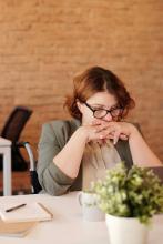 White woman at desk with head down and hands clasped